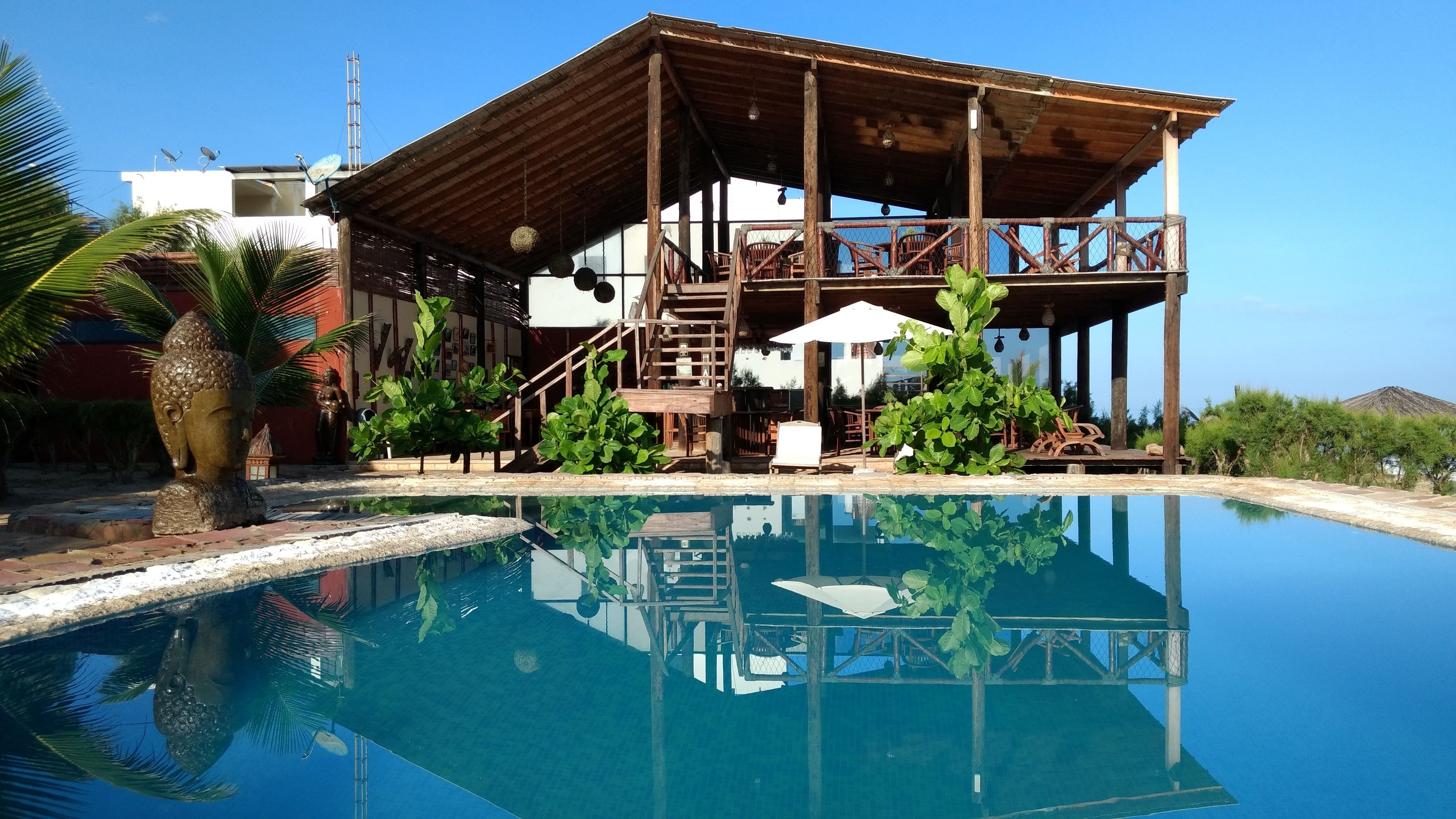 Edificio de madera con piscina, rodeado de follaje y un cielo despejado.