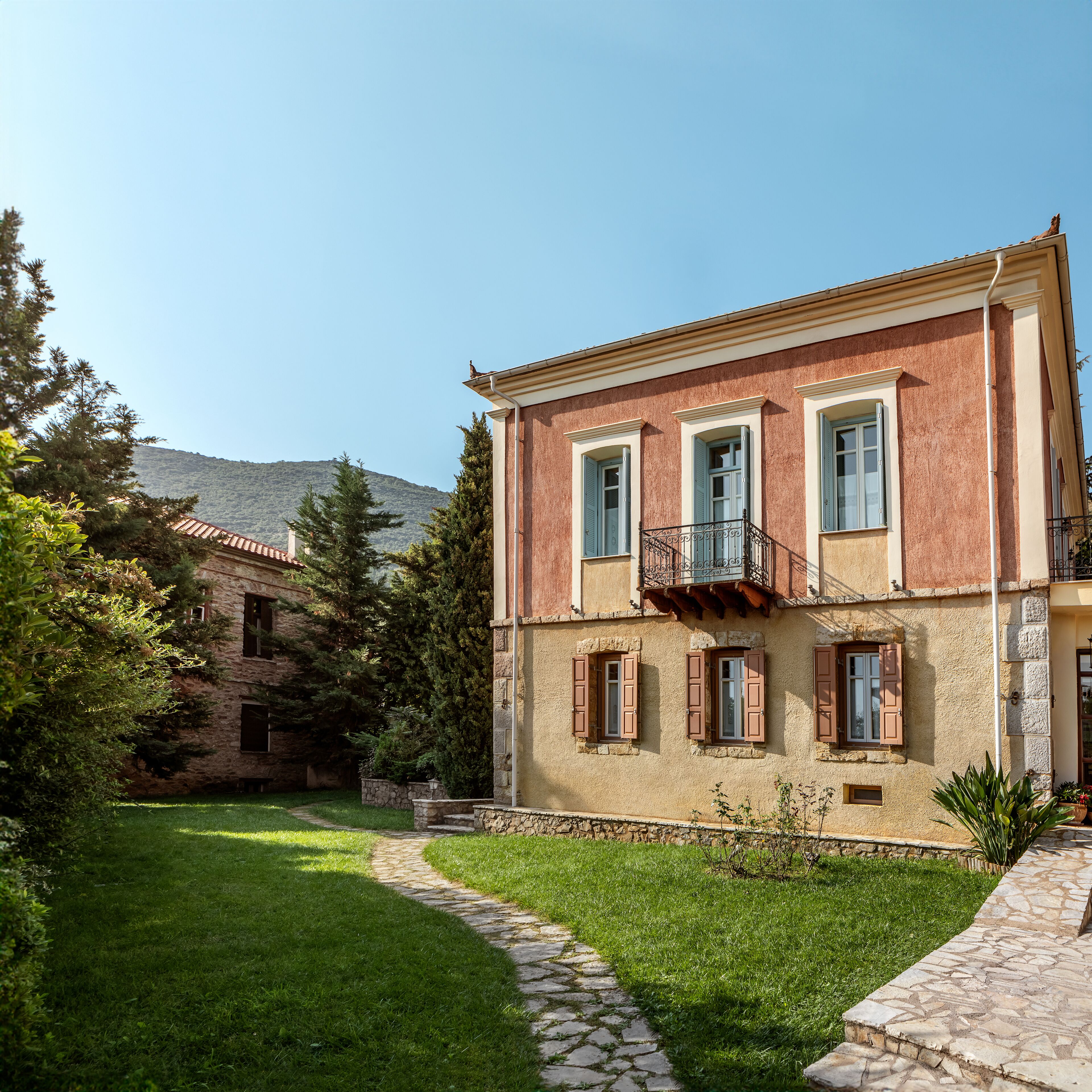 A two-story building with a stone facade, a balcony with metal railings, and a stone pathway leading to the entrance.