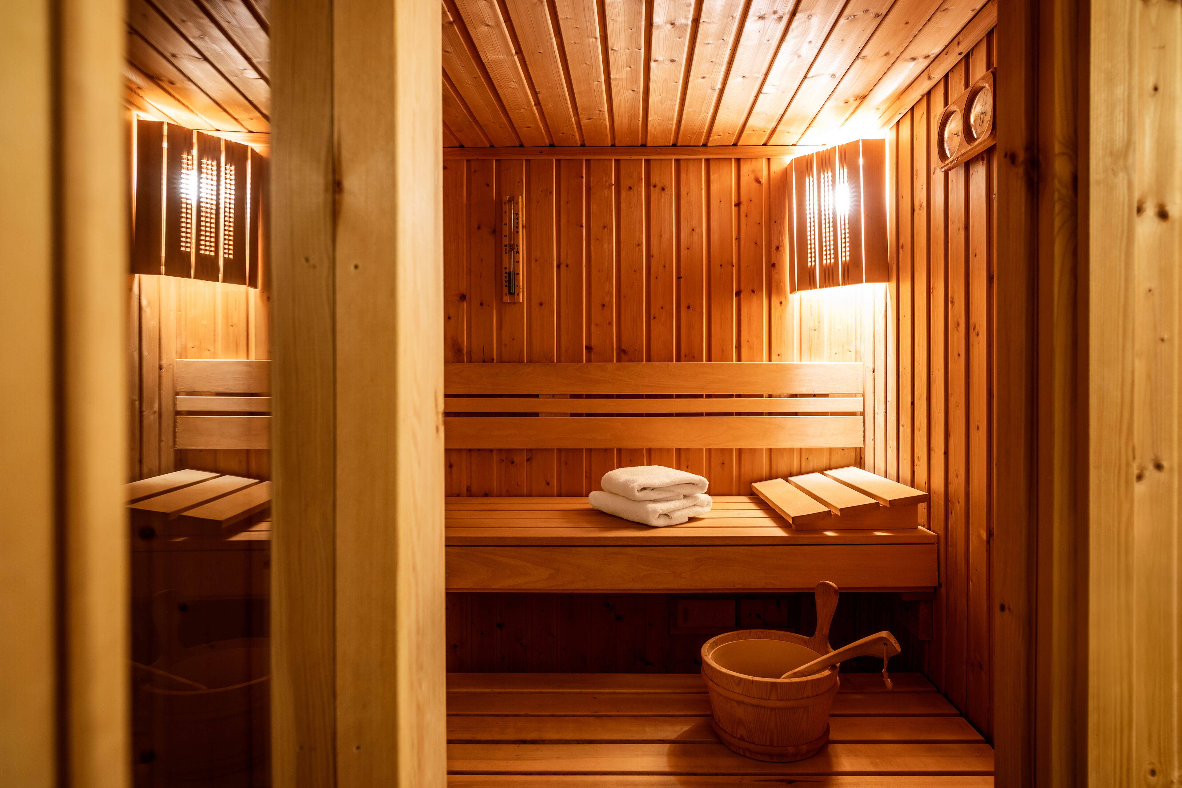 A wooden sauna with benches, a towel, and a wooden bucket.