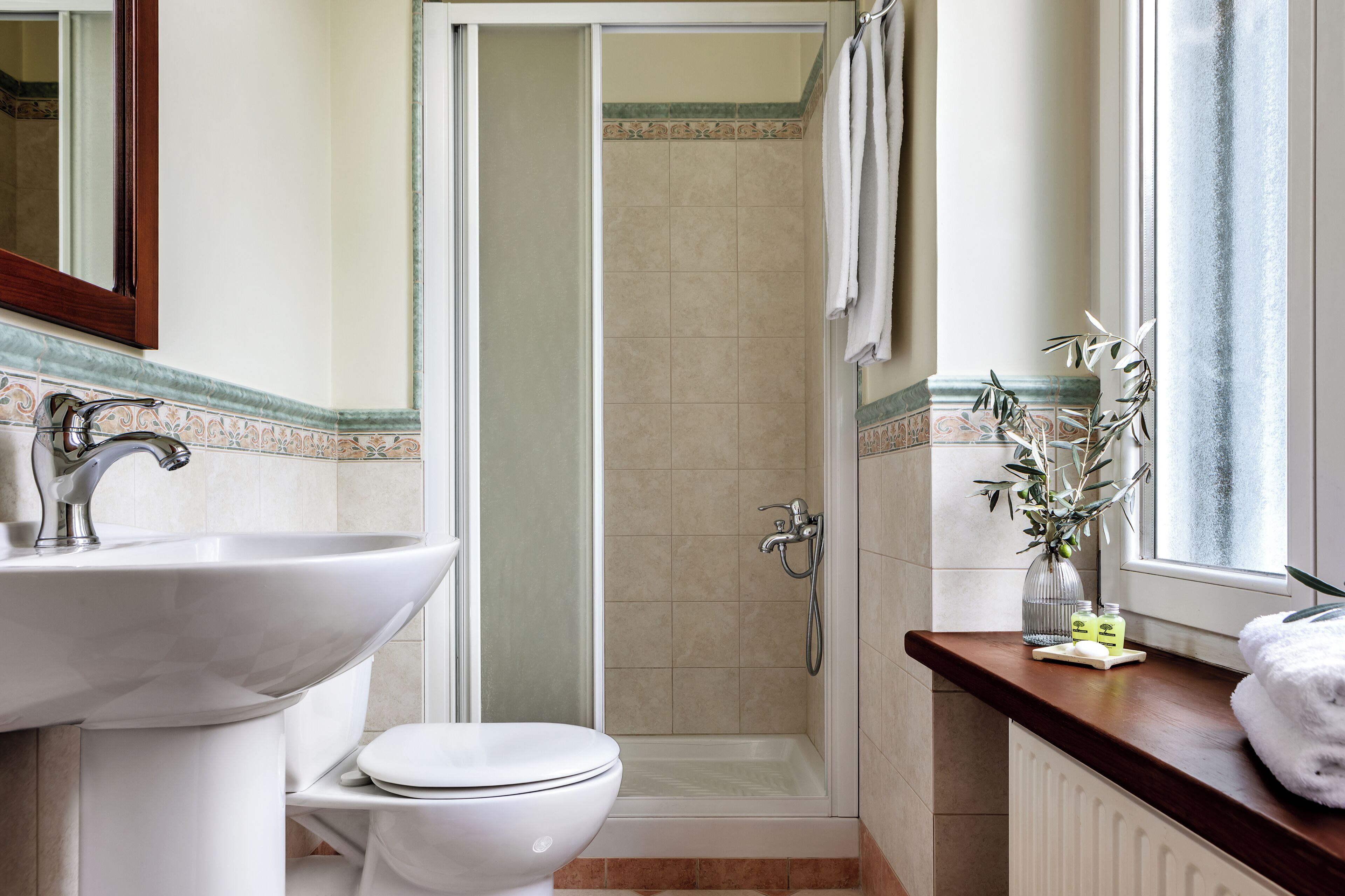 Une salle de bain équipée d’un lavabo, de toilettes, d’une douche et d’une fenêtre donnant sur un paysage agréable.