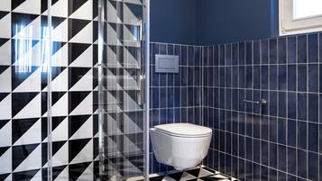 Un bagno con pavimento a scacchi bianchi e neri, cabina doccia in vetro e un water su una parete rivestita di piastrelle blu.