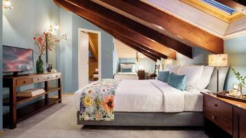 A bedroom with a bed, bedside table, lamp, and a desk with a TV.