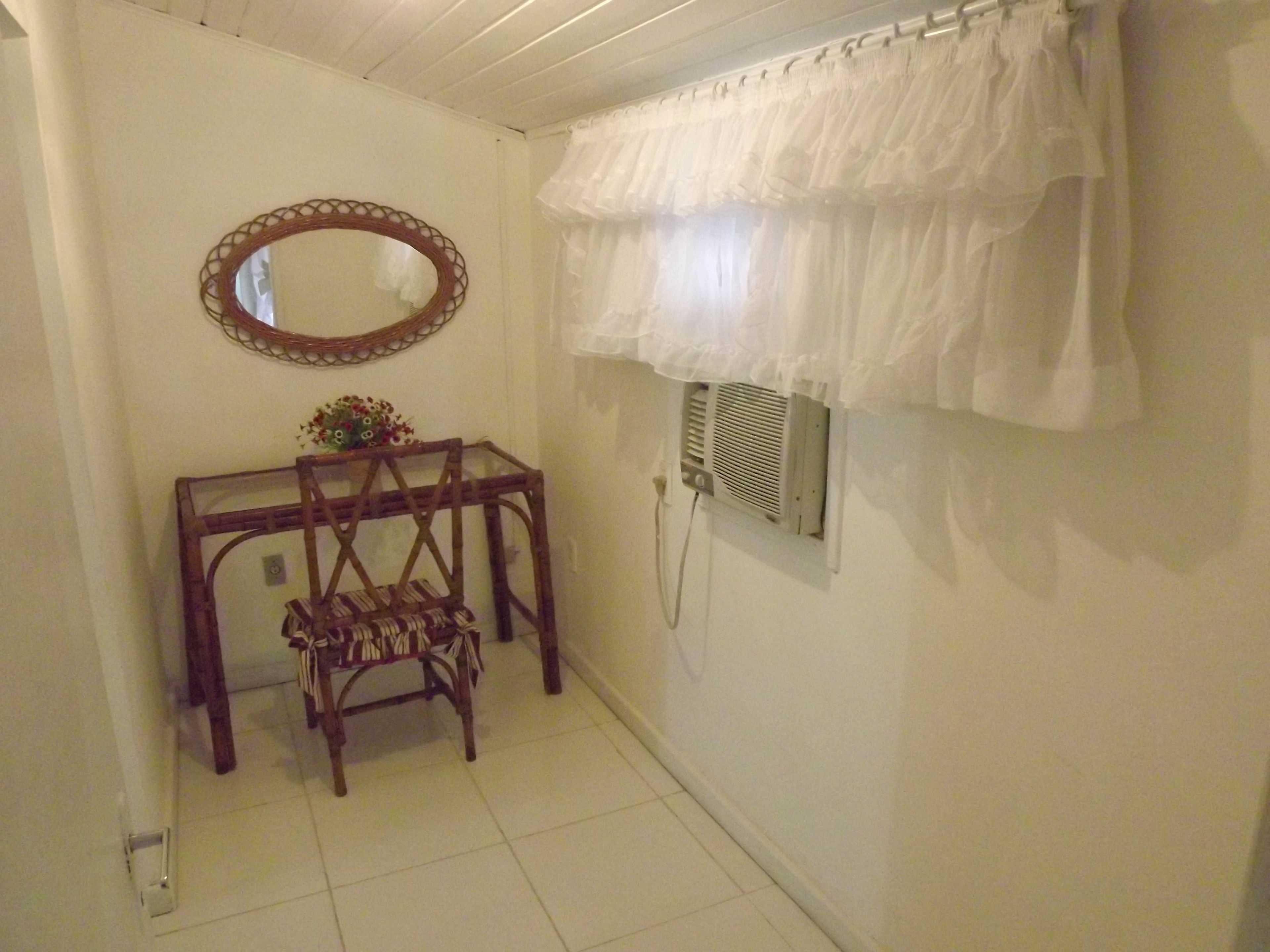 A small, clean bathroom with a wooden chair, a mirror, a radiator, and a white shower curtain.