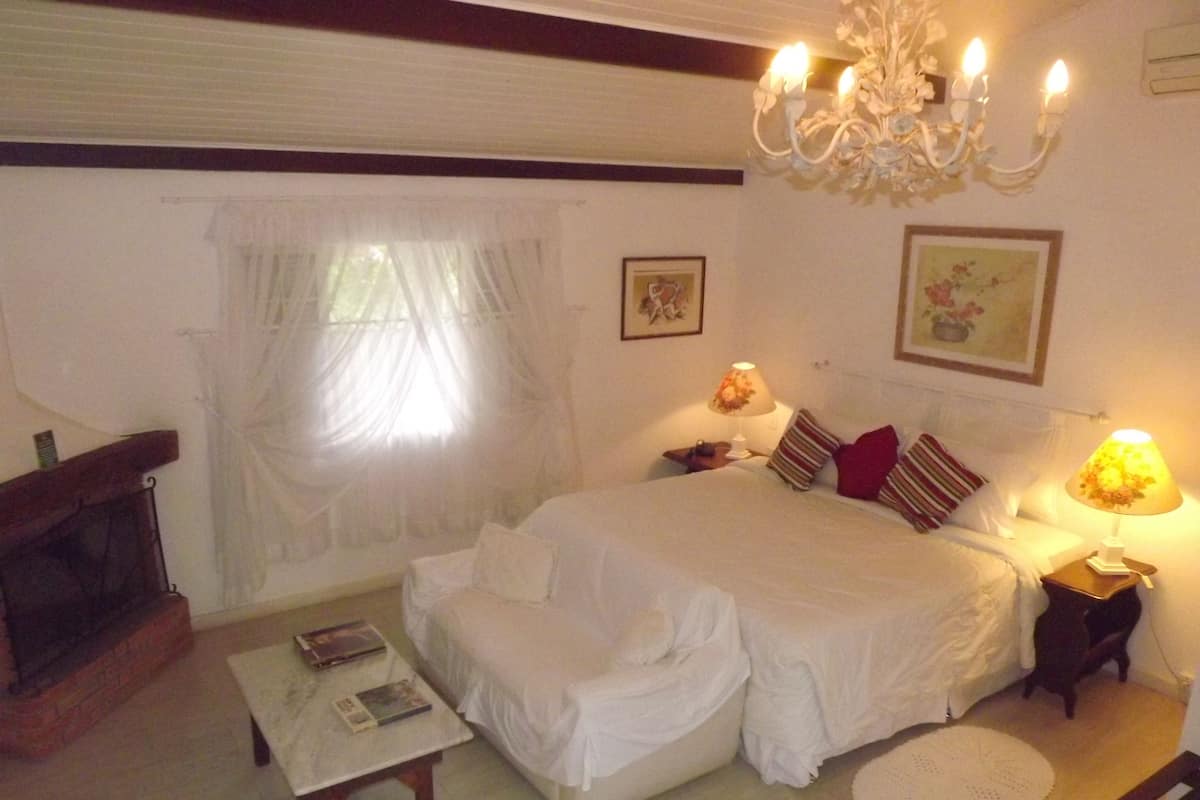 Ein Schlafzimmer mit einem großen Bett, einem kleinen Tisch, einem Stuhl, einer Chandelieber und einem Kamin.