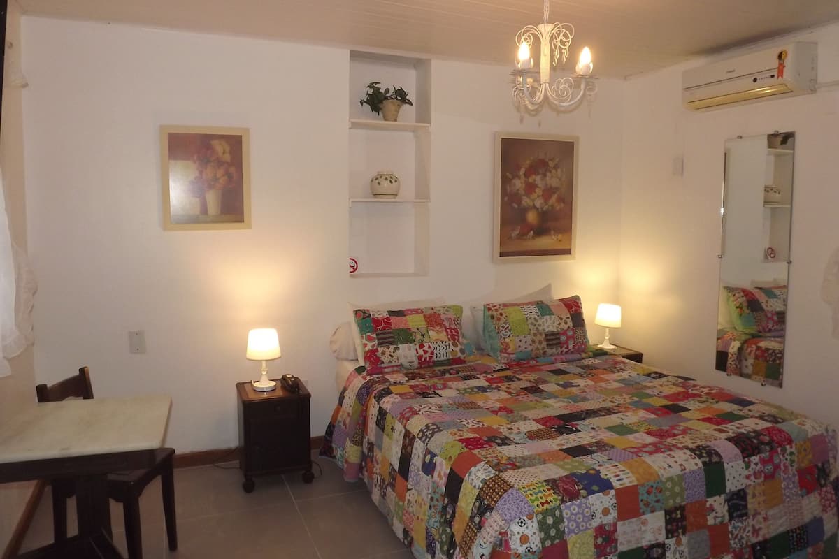 Ein Schlafzimmer mit einem Bett, zwei Nachttischen, einem Schreibtisch, einem Stuhl, einer Deckenleuchte, einem Spiegel und Wandgestaltungen.