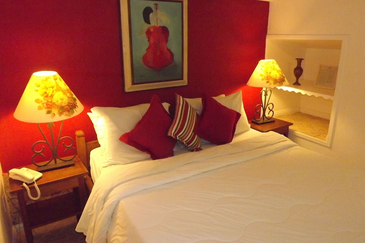 Ein Hotelzimmer mit einem Bett, zwei Nachttischlampen, einem Telefon, einem Bild an der Wand und einem Fenster mit Blick.