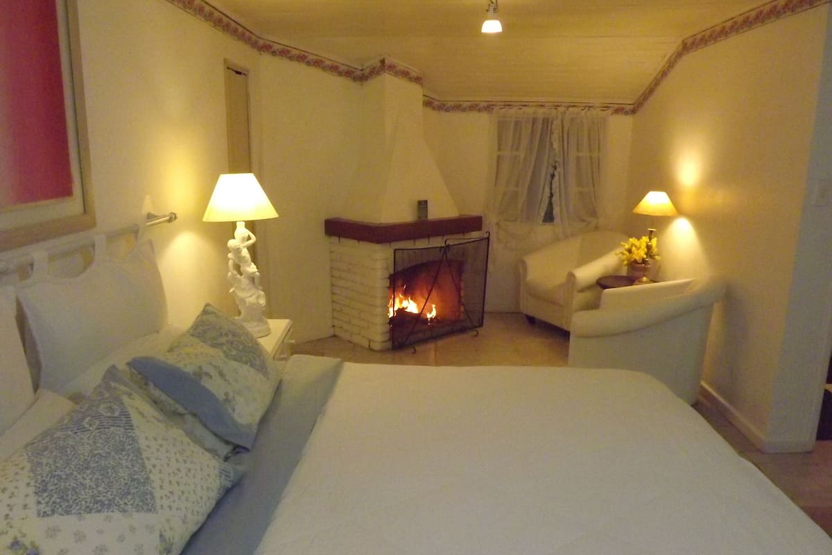 Ein Schlafzimmer mit Bett, Kamin, Sessel und zwei Lampen.