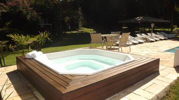 A hot tub with a wooden frame, surrounded by a patio area with chairs and a table.