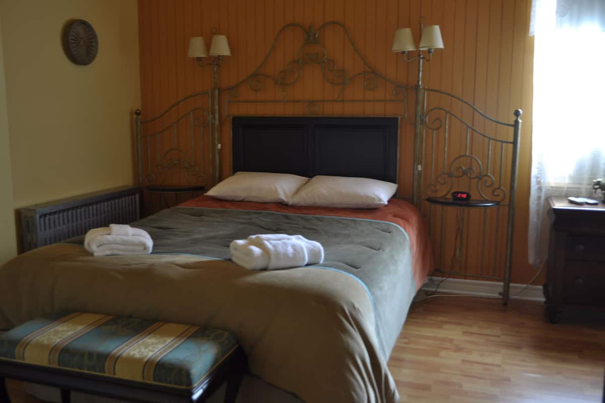 Una cama bien hecha con almohadas y una colcha, una mesita de noche con lámpara, y un banco al pie de la cama.
