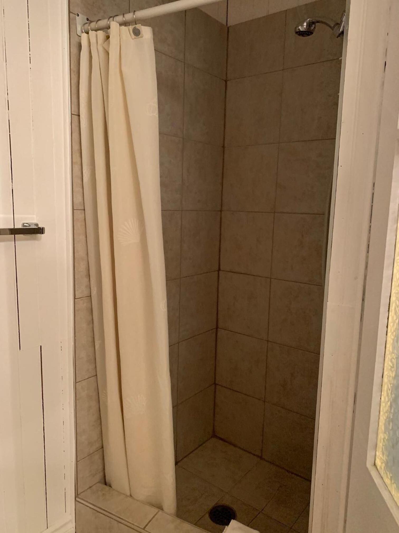 A shower area with beige tiles, a white door, and a shower curtain.