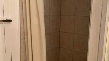 A shower area with beige tiles, a white door, and a shower curtain.