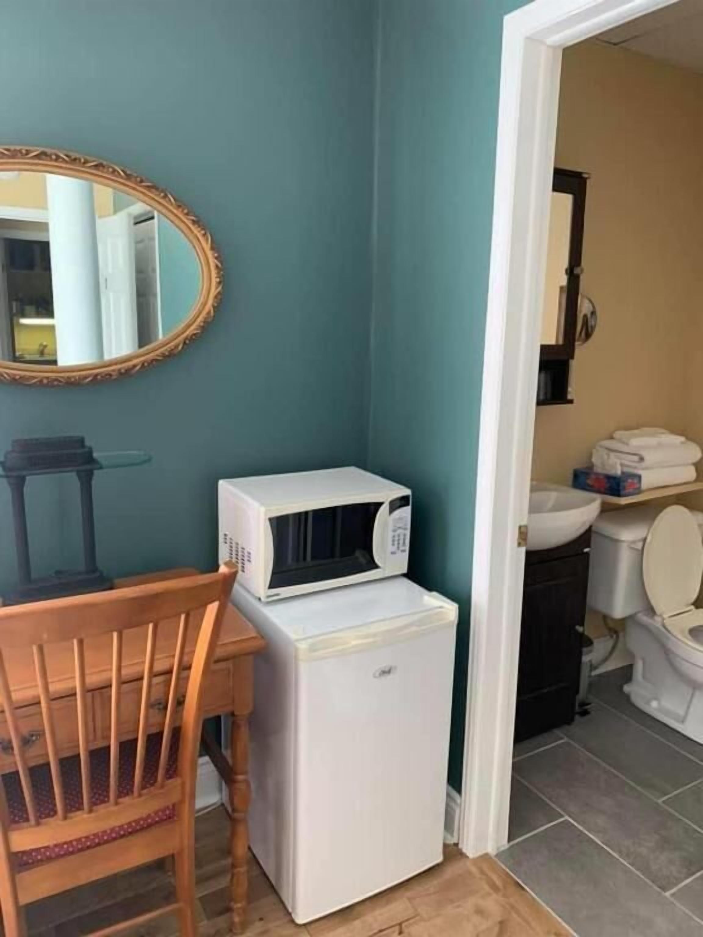 A compact kitchenette with a microwave and refrigerator, a wooden chair, and a mirror on teal walls.