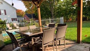 An outdoor patio with a glass-top table and wicker chairs, surrounded by a wooden pergola. - Gîte Le Roupillon en Beauce (Scott)