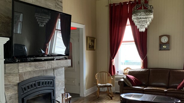 A living room with a fireplace, a television, a chandelier, a sofa, and a coffee table. - Gîte Le Roupillon en Beauce (Scott)