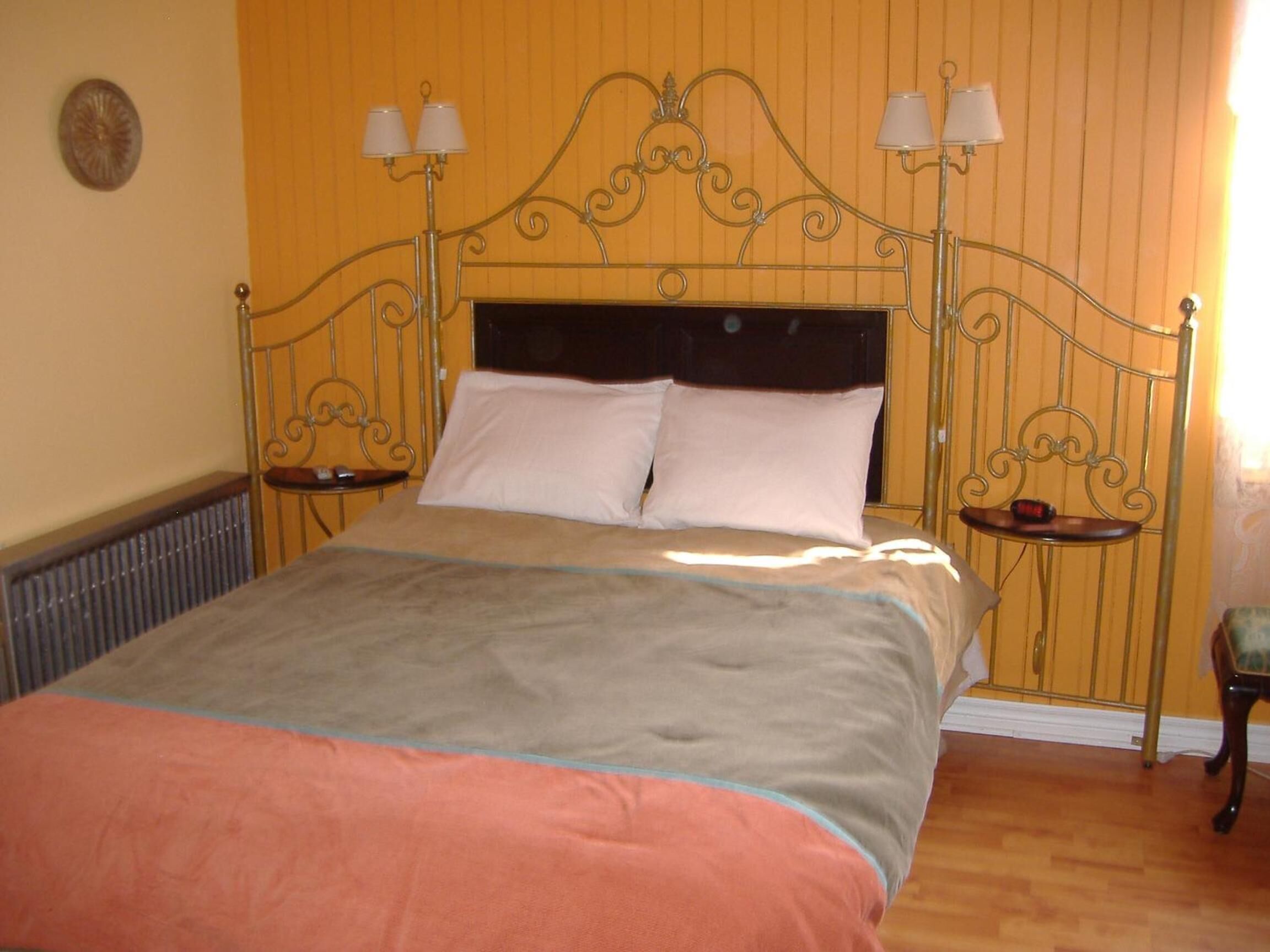 Una cama con cabecera metálica, dos mesitas de noche con lámparas y suelo de madera.