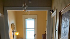 A hallway with a wooden floor, a chair, a lamp, and a door leading to another room. - Gîte Le Roupillon en Beauce (Scott)