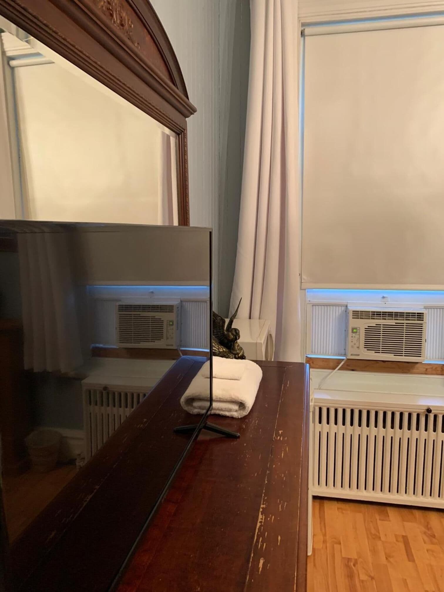 A room with a wooden dresser, a mirror, a radiator, and a window with curtains.