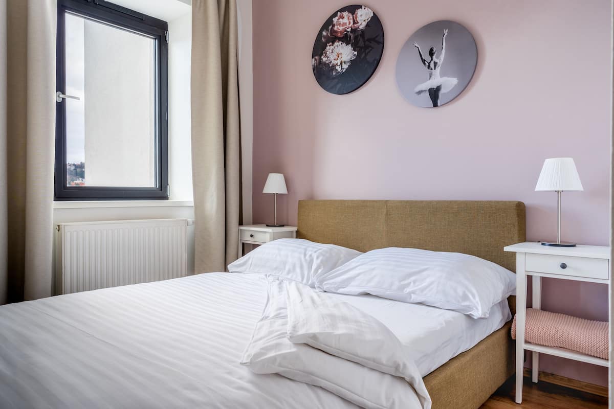 A neatly made bed with white linens, a wooden headboard, and two bedside tables with lamps.