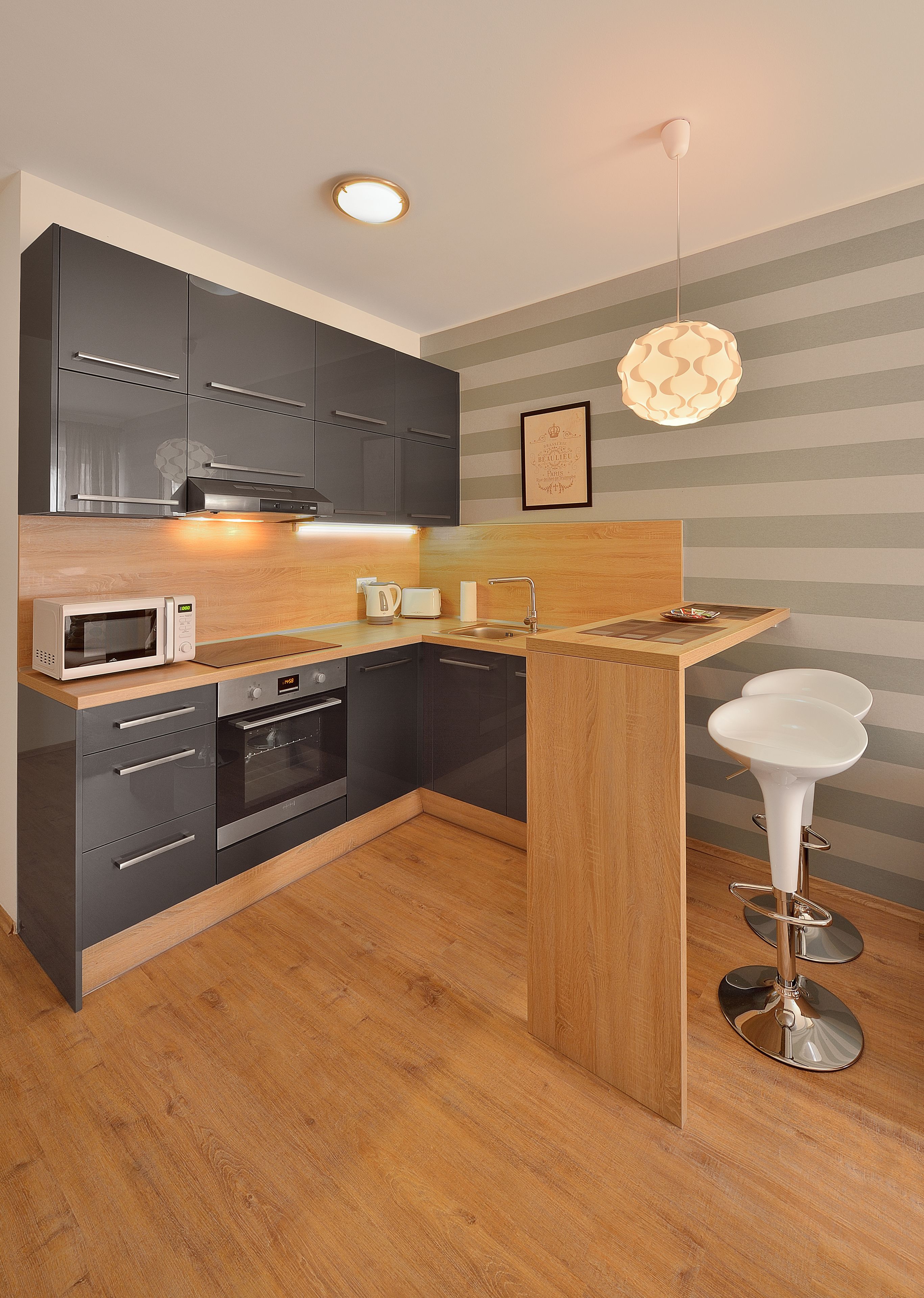 A modern kitchen with grey cabinets, a wooden countertop, a microwave, an oven, a sink, and a bar stool.
