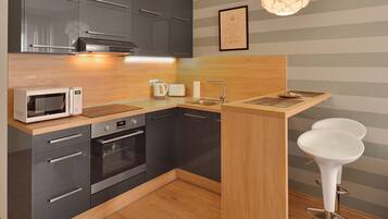 A modern kitchen with grey cabinets, a wooden countertop, a microwave, an oven, a sink, and a bar stool.