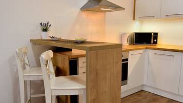 A compact kitchen with a wooden island, white cabinets, a microwave, and two white chairs.