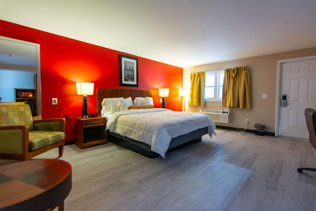 Quarto de hotel com cama, duas luminárias laterais, uma cadeira, escrivaninha e janela com cortinas.