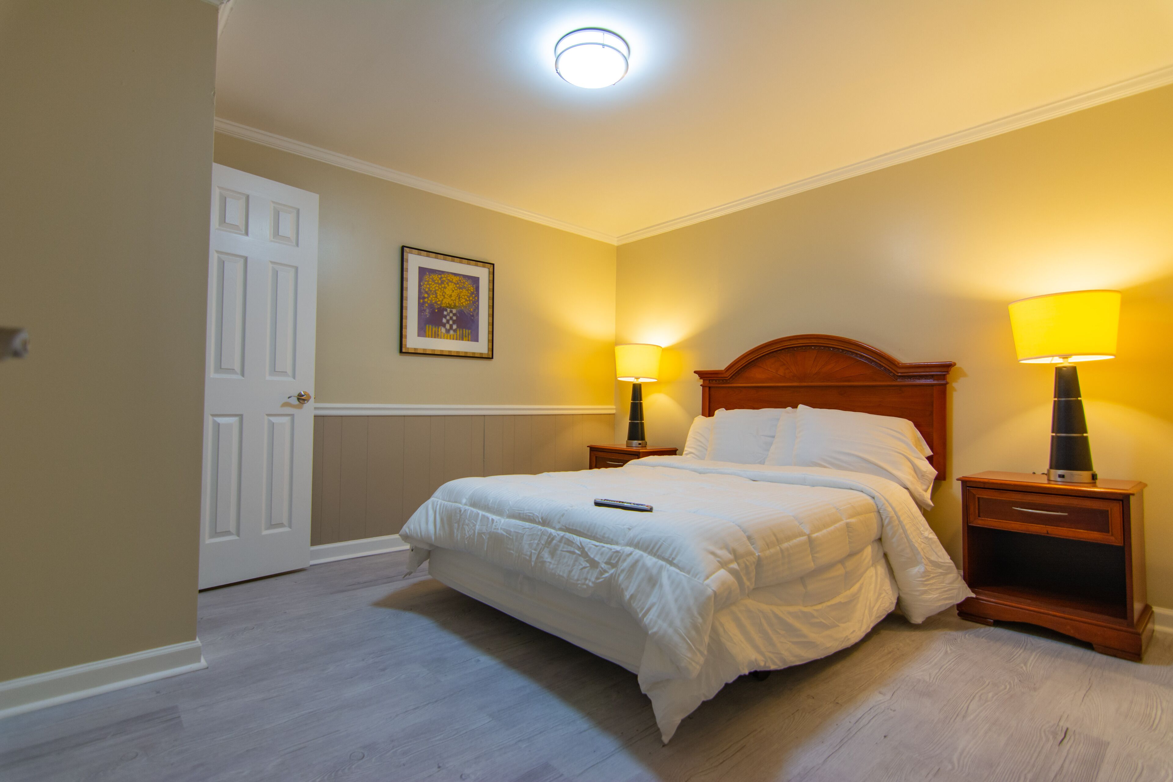 A bedroom with a double bed, two bedside tables with lamps, a door, and a framed picture on the wall.