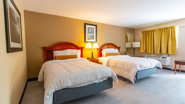A hotel room with two beds, a bedside table with lamps, a mirror, a window with yellow curtains, and a framed picture on the wall. - Eden Inn Motel (Eden)