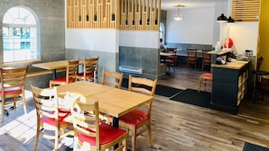 Interior moderno de restaurante con mesas y sillas de madera, un panel de madera central y vista al exterior a través de un amplio ventanal.
