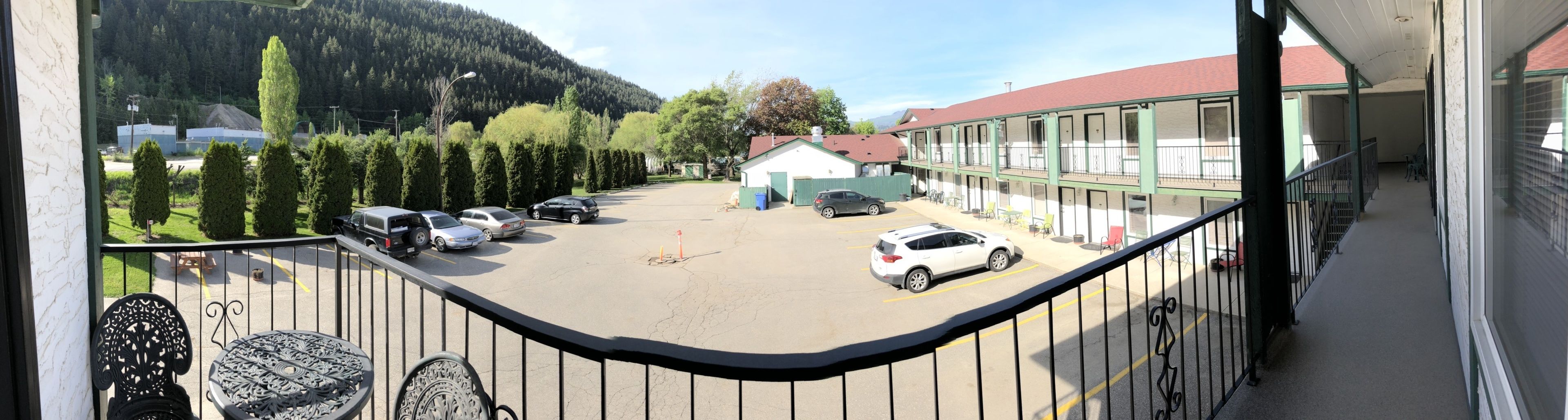 A hotel with a parking lot, a building with a red roof, and a mountain in the background.
