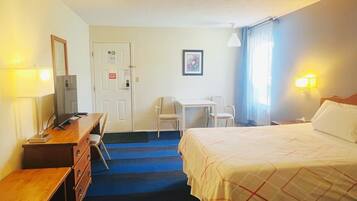 A hotel room with a bed, desk, chair, dresser, and a door with a sign.