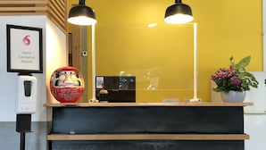 Una recepción con diseño de listones de madera, una estación de higiene para manos, una máscara decorativa roja y una planta en maceta.