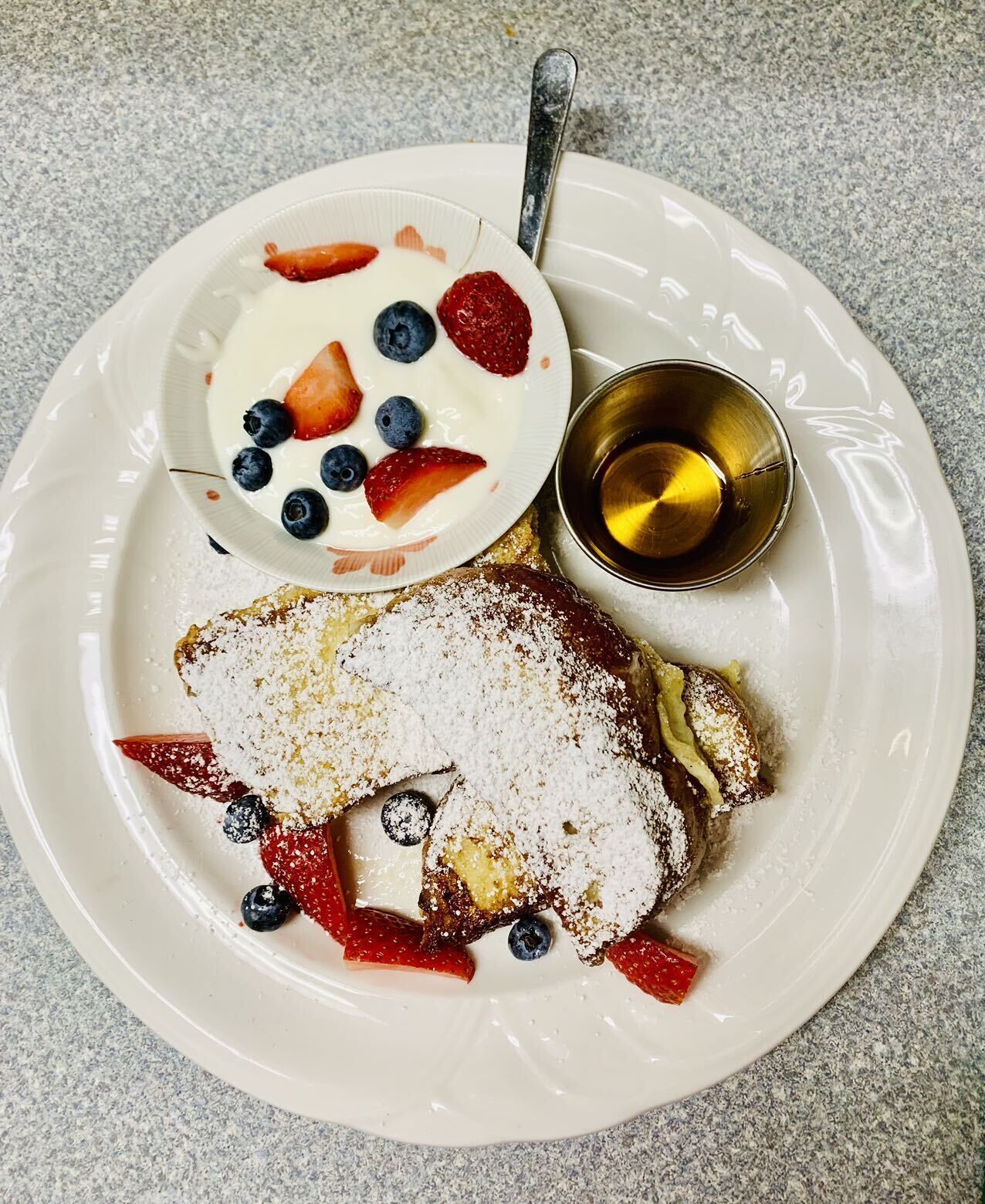 Un plato de panqueques, un tazón de yogur con bayas y una taza pequeña de jarabe.