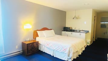 A hotel room with a bed, bedside table, lamp, kitchenette, and a blue carpet.