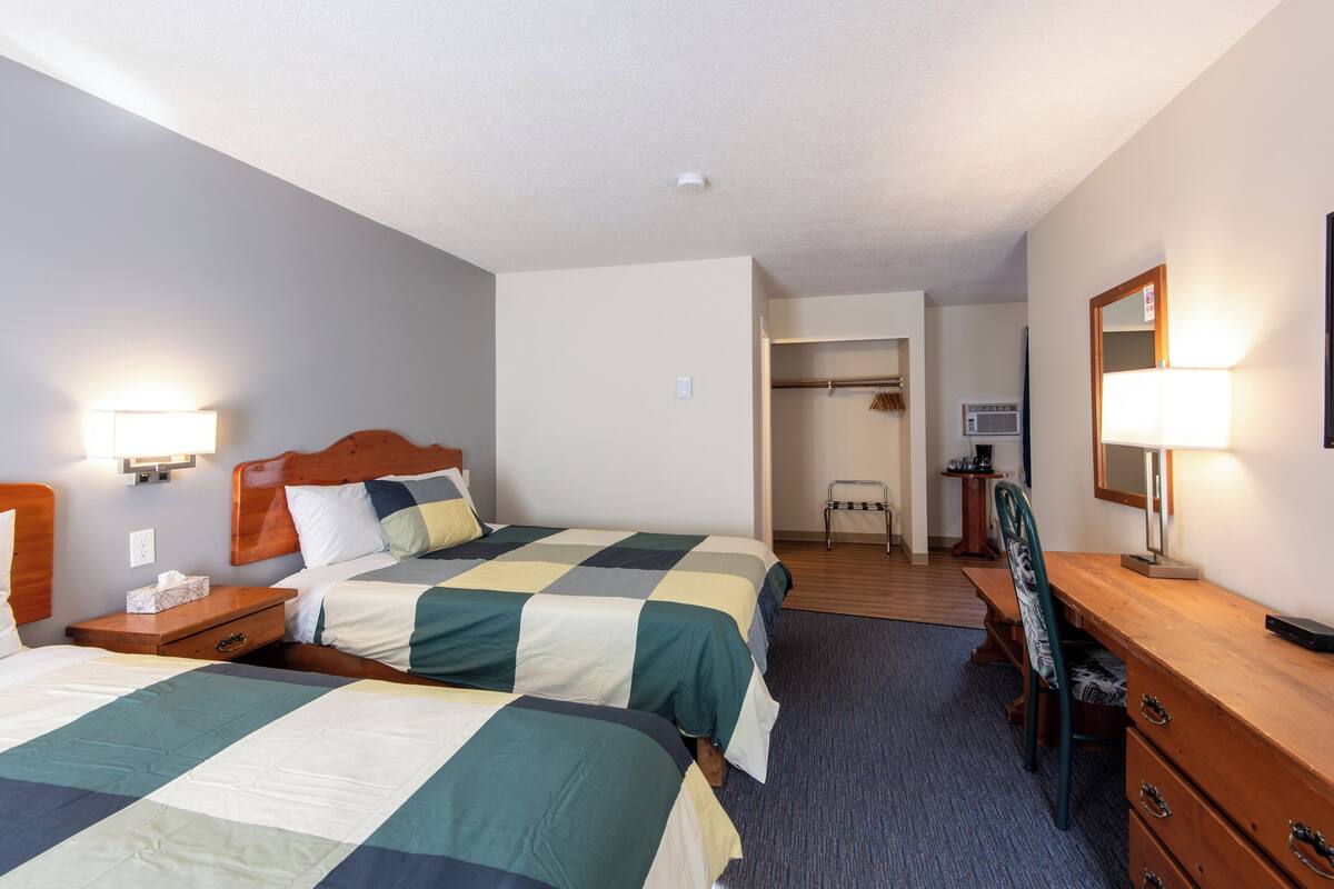 A hotel room with two beds, a desk, a chair, a mirror, and a walk-in closet.