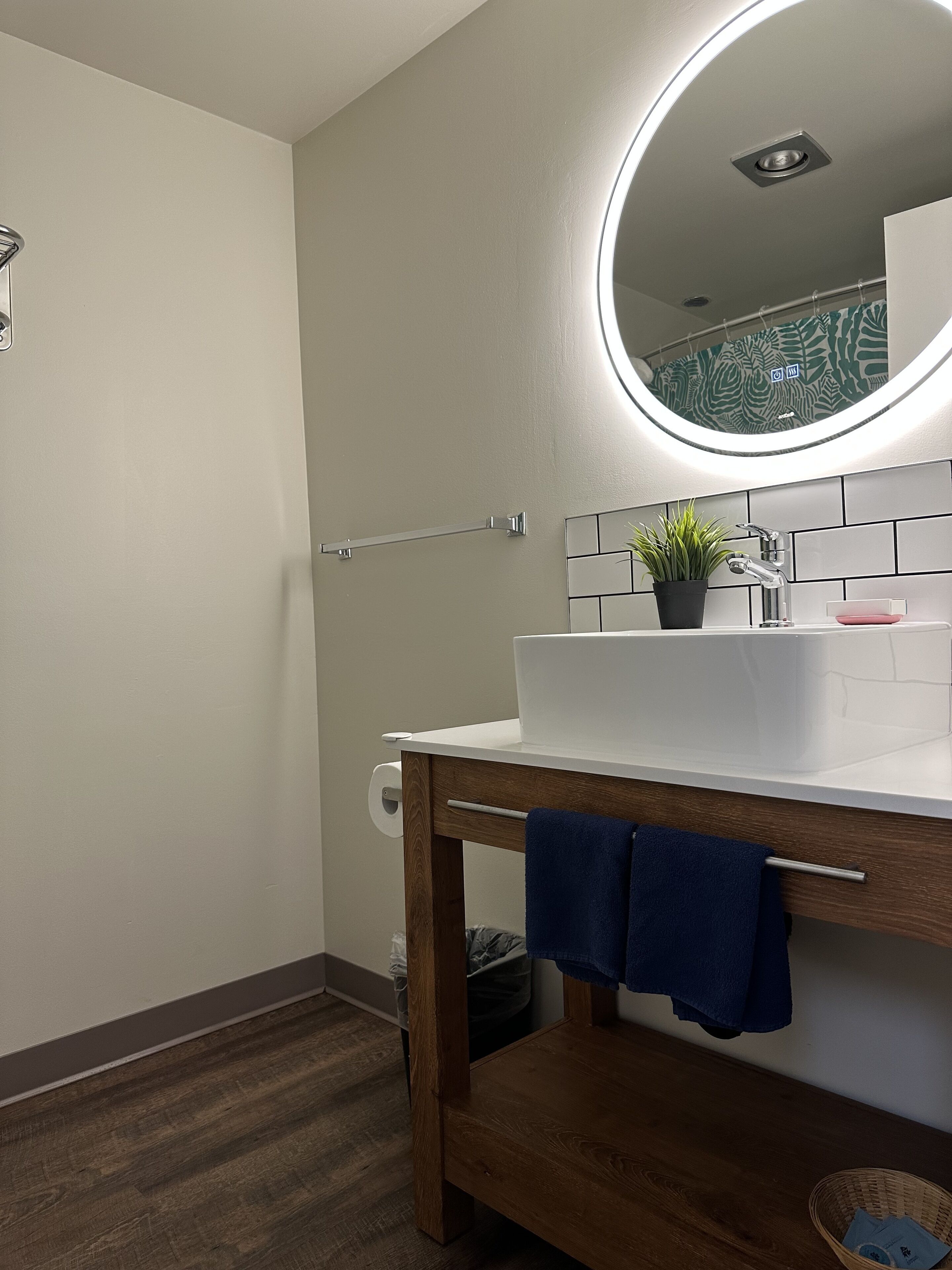 A bathroom with a white sink, a mirror with a light, a towel rack, and a wooden vanity.