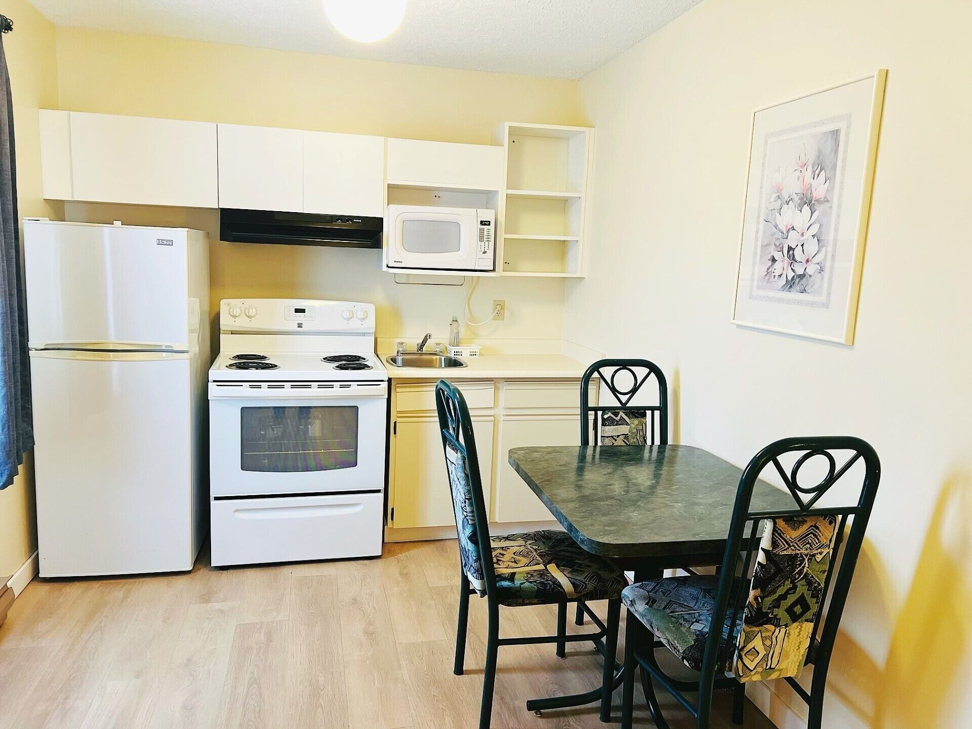 Una cocina compacta equipada con refrigerador, estufa, microondas y una mesa de comedor con sillas.