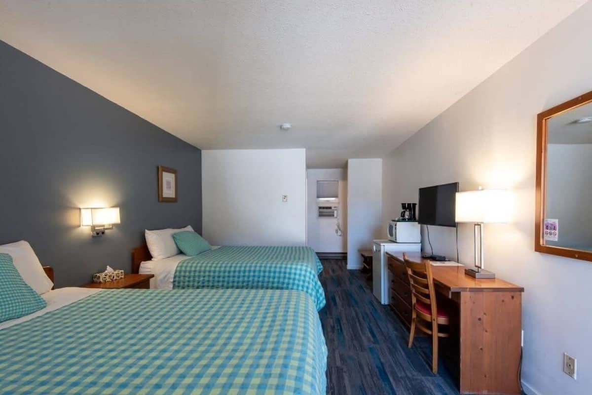 A hotel room with two beds, a desk, a chair, a TV, and a mirror.