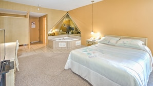 A bedroom with a large bed, a sitting area with a chair and table, a small bathroom with a bathtub, and a mirror reflecting the room. - Hotel Motel Penn - Mass (Trois-Rivieres)
