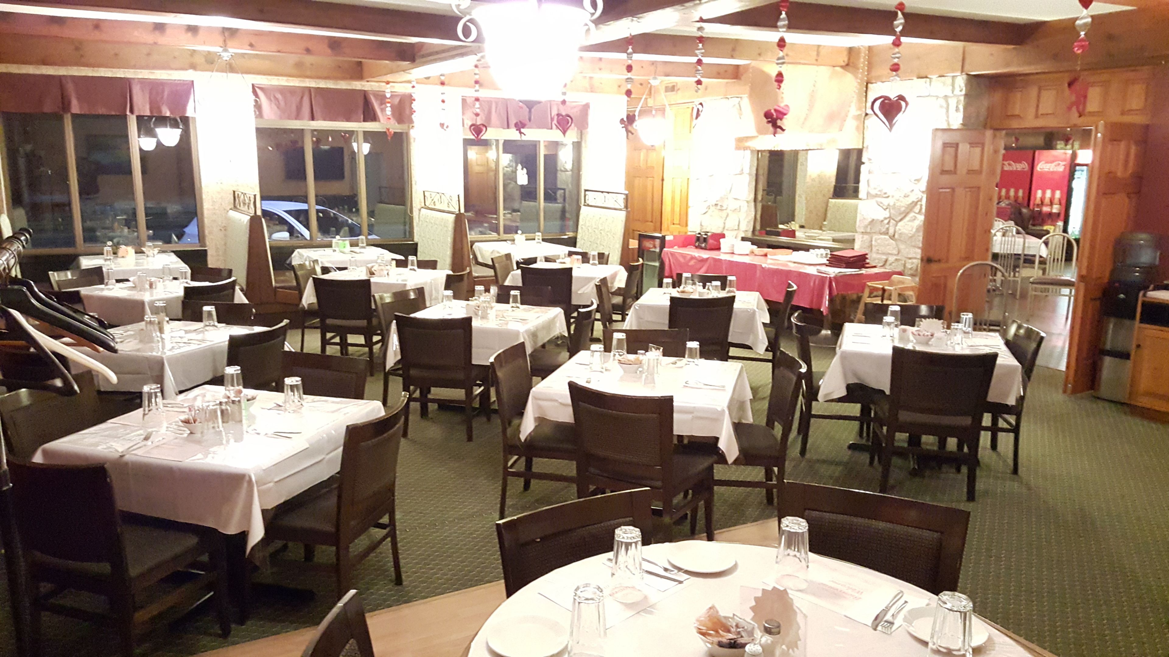 Un restaurante con varias mesas preparadas para comer, paredes de madera y una cocina visible al fondo.