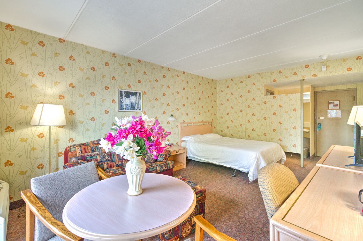 Una habitación de hotel con una cama individual, una mesa redonda con un florero, un sofá y un escritorio.