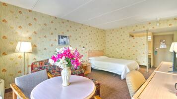 Una habitación de hotel con una cama individual, una mesa redonda con un florero, un sofá y un escritorio.