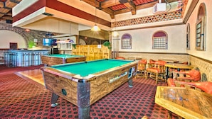 A pool table in a room with a red patterned carpet, wooden furniture, and a bar area with a television. - Hotel Motel Penn - Mass (Trois-Rivieres)