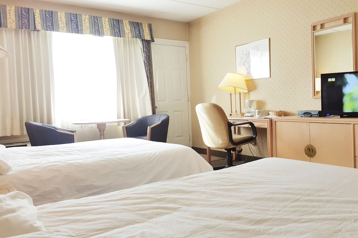 A hotel room with two beds, a desk with a lamp, a television, and a chair.