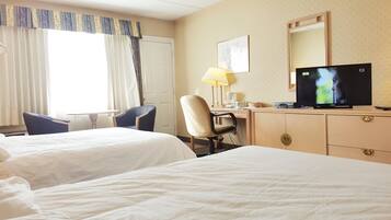 A hotel room with two beds, a desk with a lamp, a television, and a chair.