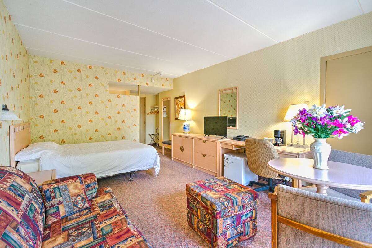 A hotel room with a bed, a desk, a chair, a small table, and a decorative vase.