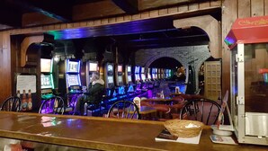 A bar with multiple gaming machines, a menu board, and a person seated at a table. - Hotel Motel Penn - Mass (Trois-Rivieres)