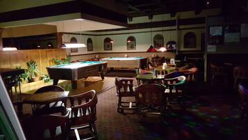 A billiards room with a pool table, chairs, and tables.