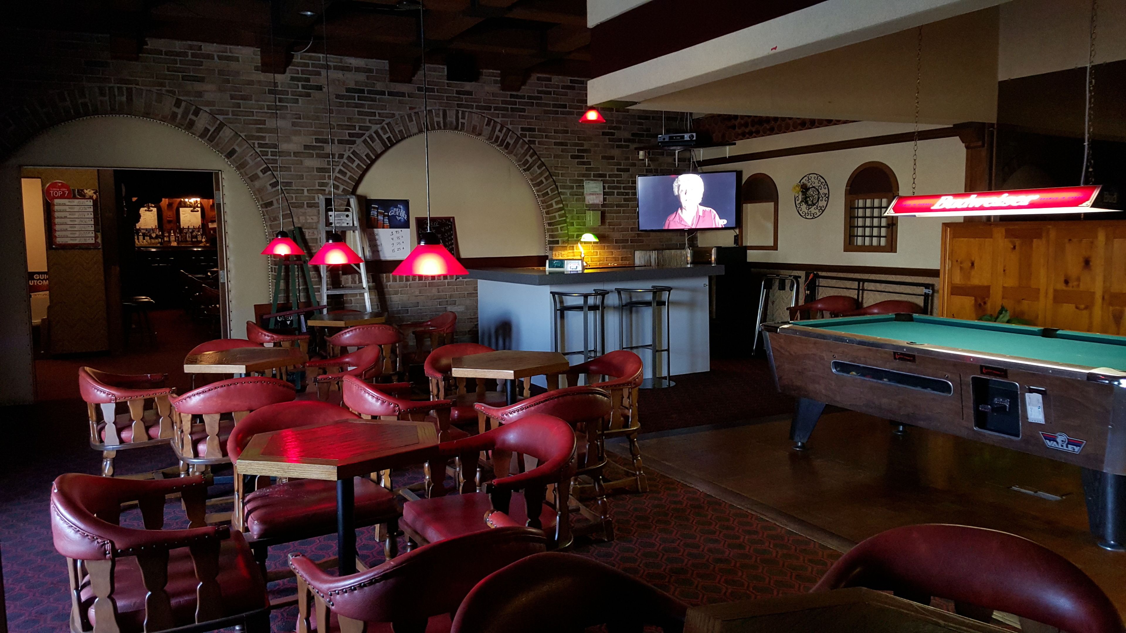 Zona de bar amb cadires de cuir vermell, taula de bitlles i pantalla de televisió.
