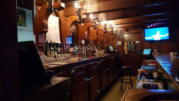 A bar area with wooden decor, a TV screen, and various bottles and glasses. - Hotel Motel Penn - Mass (Trois-Rivieres)